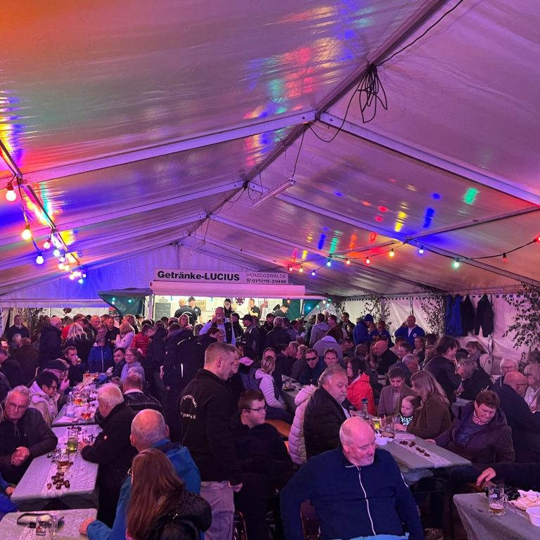 Voller Festzelt mit vielen Menschen, bunten Lichtern und Tischen.