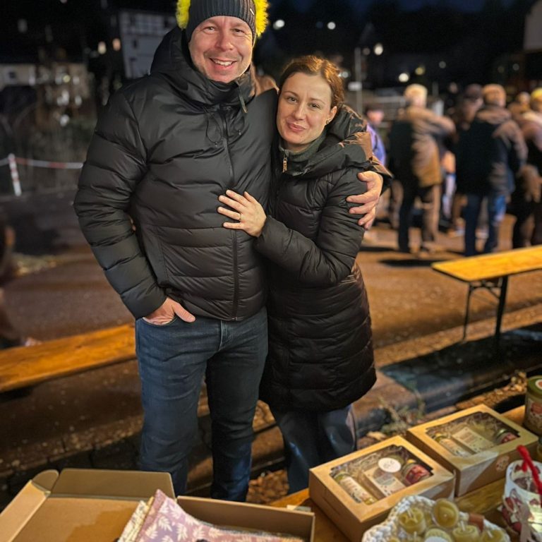 Paar in Winterkleidung lächelt an einem Marktstand mit Honigprodukten