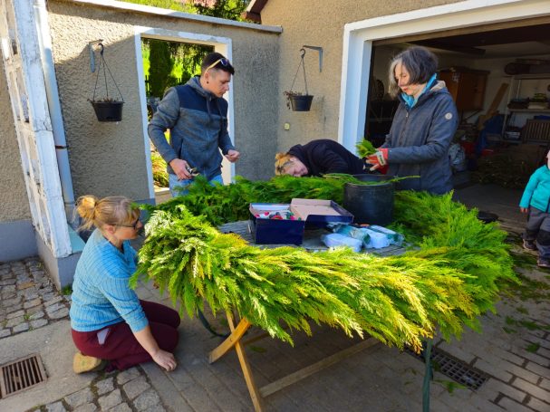 Gemeinschaftliches Arbeiten an einem großen, grünen Kranz im Freien.