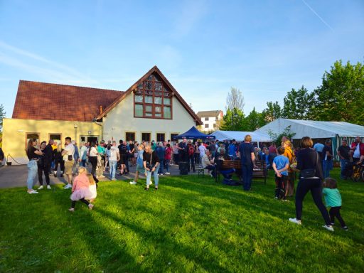 Menschenmenge beim Fest, mit Zelten und einem Gebäude im Hintergrund, umgeben von Grünflächen.