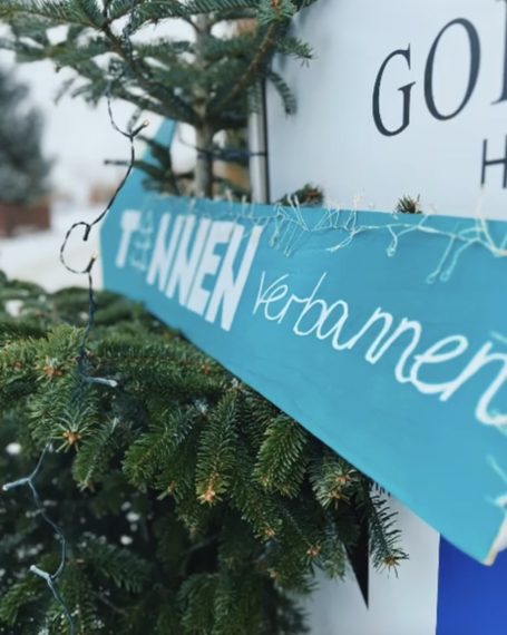 Blaues Holzschild mit der Aufschrift "WHEN Verbannten" an einem Tannenbaum.