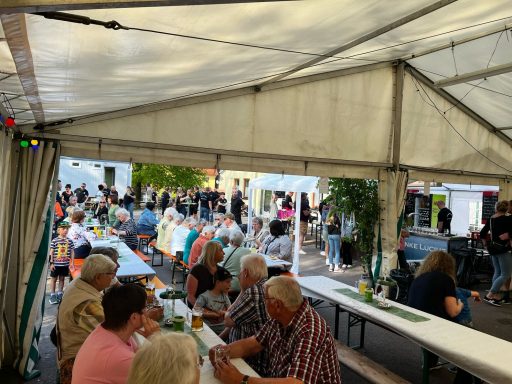 Menschen sitzen an Tischen in einem Festzelt, Hintergrund mit Veranstaltung.