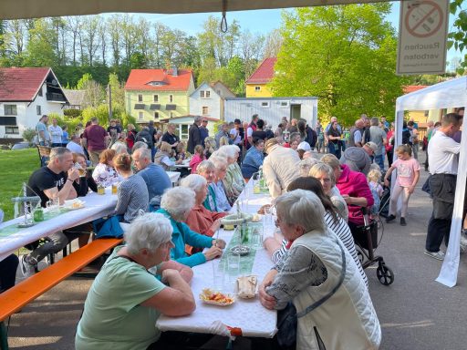 Viele Menschen sitzen an langen Tischen im Freien und genießen Essen und Getränke.