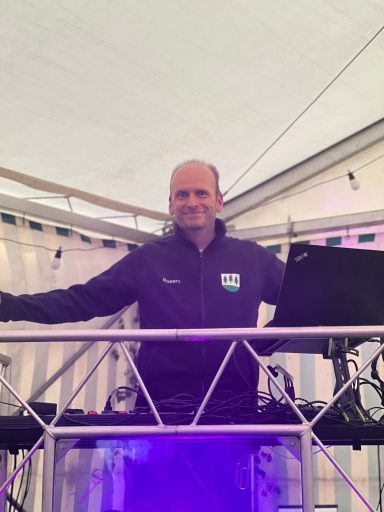 Mann steht hinter einem DJ-Pult in einem Zelt mit Lichtern und Gerätschaften.