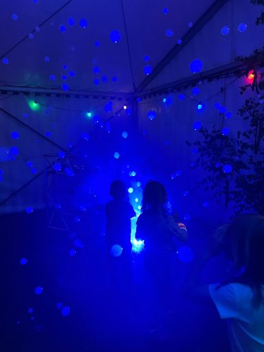 Zwei Kinder stehen in einem beleuchteten Raum mit blauen und grünen Lichtern.