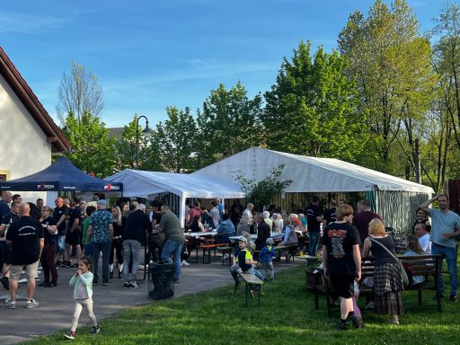 Bunte Menschenmenge auf einem Fest mit Zelten und Bänken im Freien.