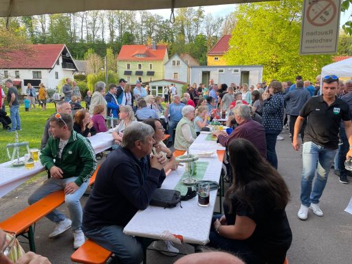 Menschenmenge bei einer festlichen Veranstaltung im Freien mit Tischen und Bänken.