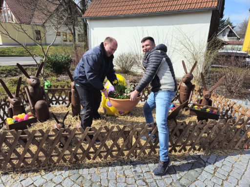 Zwei Männer dekorieren einen Osterplatz mit Hasen und bunten Eiern.