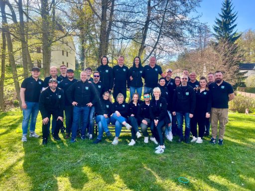 Gruppenfoto von Menschen in schwarzer Kleidung im Freien bei sonnigem Wetter.