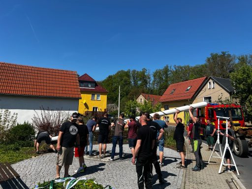 Gruppe von Personen auf einem Grundstück mit Häusern und einem Feuerwehrauto im Hintergrund.