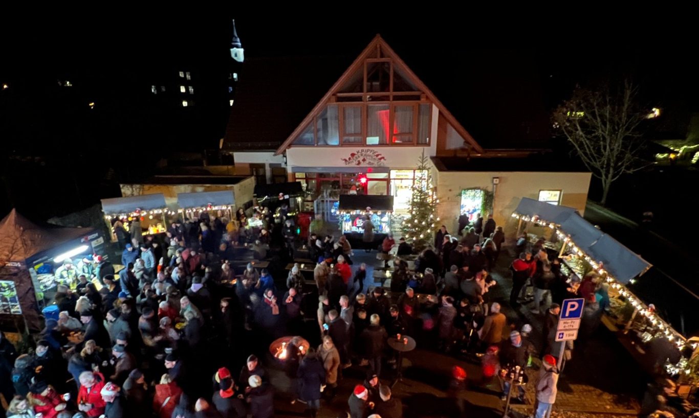 Festlicher Marktplatz bei Nacht mit vielen Besuchern und Weihnachtsständen.