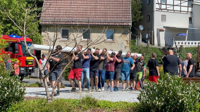 Mehrere Personen stehen auf einem Platz, während sie einen langen Gegenstand zusammenhalten.
